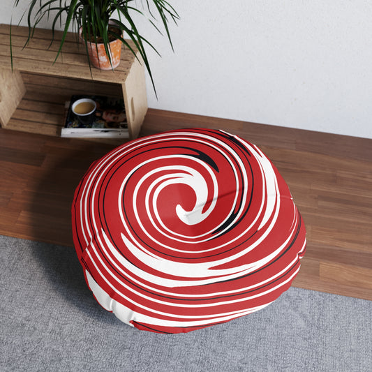 Round red and white striped cushion on a wooden floor with a plant and small table in the background.