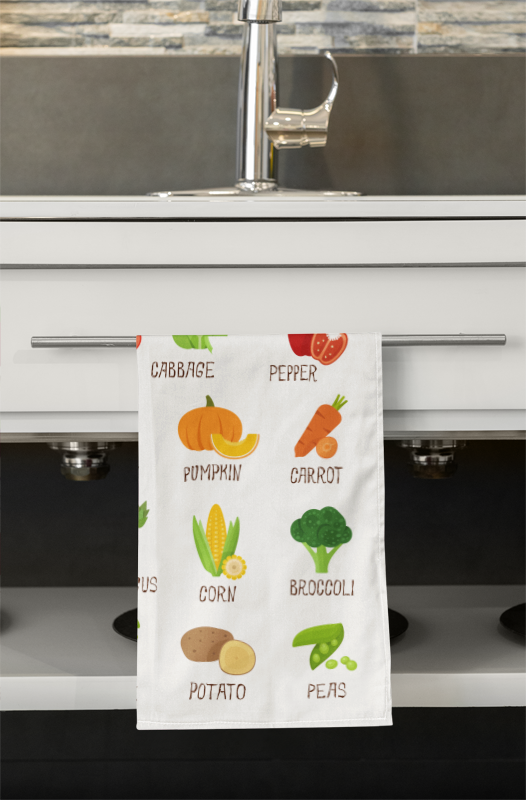 Kitchen towel with vegetable illustrations hanging on a kitchen cabinet.
