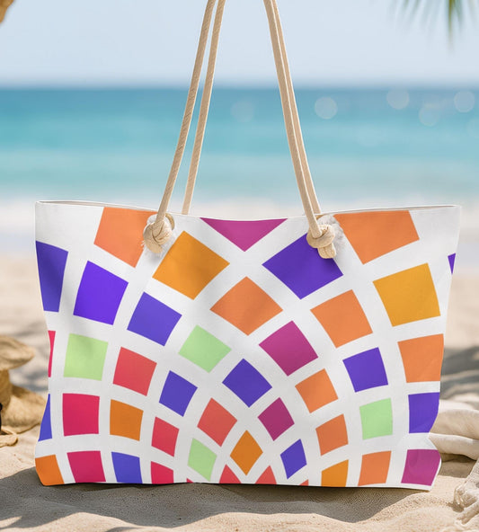 Colorful patterned tote bag on a sandy beach with a straw hat and sunglasses.