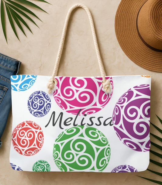 Colorful patterned tote bag with 'Melissa' branding, placed on a beige surface with a hat and jeans.